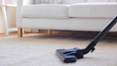 people, housework and housekeeping concept - woman with vacuum cleaner cleaning carpet at home