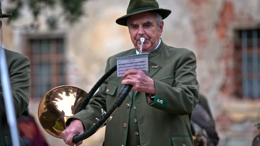 Senior hunter with hat blowing big horn. Older male person with big traditional horn playing music holding notes in one hand.