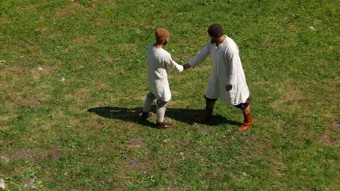 STARAYA LADOGA, RUSSIA - JULY 05, 2015: Two unidentified rustic man hold small stick by one arm, simple game competition, green grass field, arena at Viking Age performance show