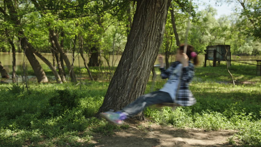 8 years old girl in plaid shirt rides a rope swing in the village in the spring in sunny weather