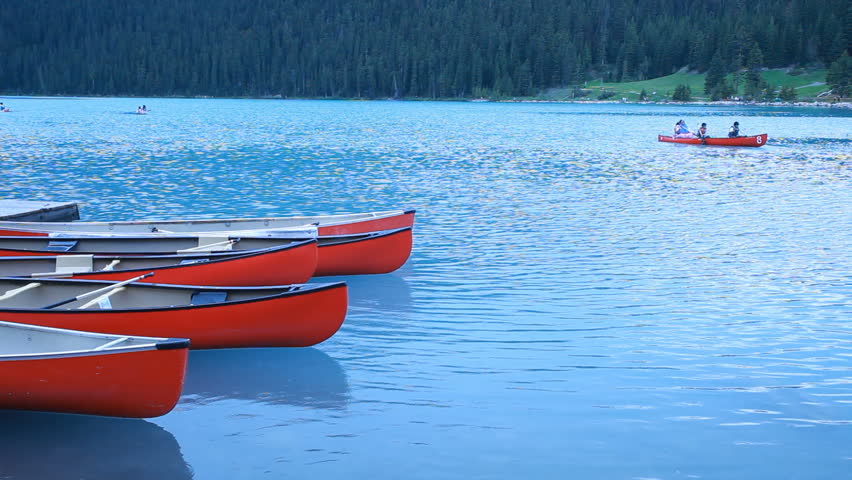 Canoes on beautiful blue lake with family floating enjoying nature and vacation, rain gently falling. Glacial blue clear water. Recreation at Lake Louise Banff National park, Alberta, Canada.