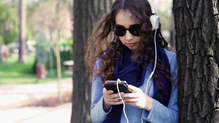 beautiful young woman in sunglasses listening to music with headphones in the park