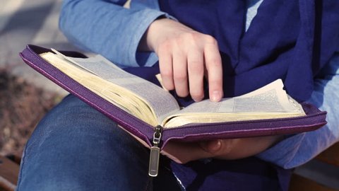 Close-up of woman's hands while reading the Bible outside