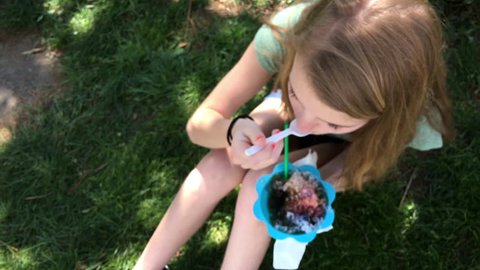 Young teenage girl eating shaved ice snow cone at summer time 4k