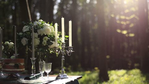 Composition of white vintage candelabrum and white roses bouquet on the wedding decorated table in the forest.  Romantic dinner in the woods 庫存影片