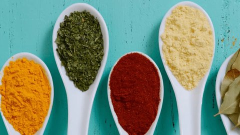 Colorful cooking spices and herbs in white spoons on vintage aqua blue table overhead, panning across and zoom out.