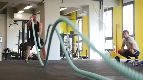 SLOW MOTION: Strong man working out with Battle Ropes in a gym. 