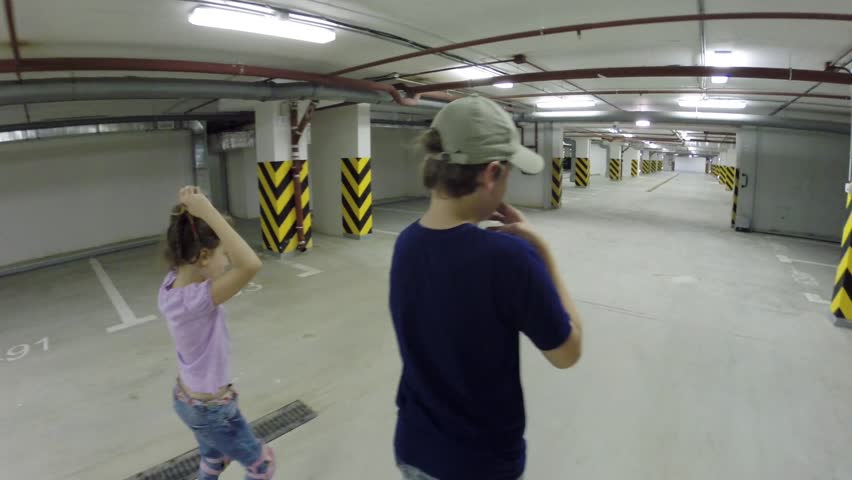 Happy girl and boy roller skate in underground parking, back view