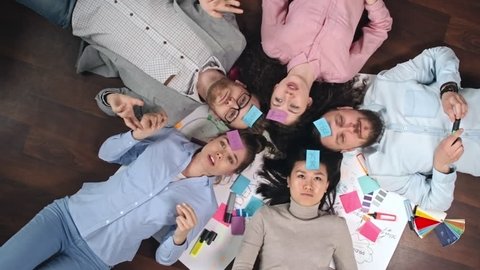 Directly above view of young team with sticky notes on their foreheads lying on floor in circle and playing Who am I game, shot on Sony NEX 700 + Odyssey 7Q