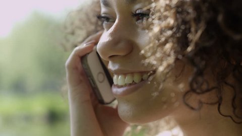 Beautiful young girl with dark curly hair using her cell phone, outdoor. Portrait of relaxed young lady in a summer park talking on phone. Arkivvideo