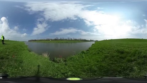 Man is Walking by a Green Lawn, Hills Around a Water, Spherical Panorama Video, vr Video 360, Little Planet Video, Video For Virtual Reality, Landscape, Man in Lemon Yellow Sporty Jacket, Lake or