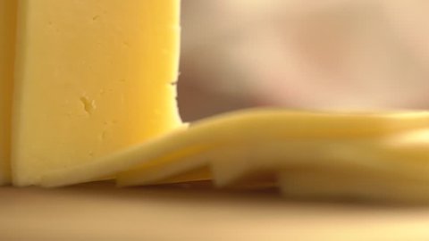 Slicing cheese into pieces closeup, super slow motion. Closeup shot of a piece of cheese. Somebody is cutting cheese with a knife. 