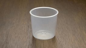 White rice streaming down and filling up clear plastic cup against dark natural wood background, slow motion