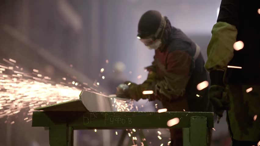 Worker using industrial grinder on metal parts in industrial workshop warehouse