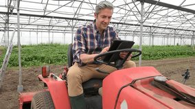 Farmer using digital tablet in greenhouse sit on tractor