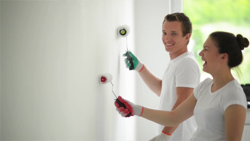 Young couple decorate their new apartment. Young husband and wife are painting the wall. Beautiful couple making repairs in their new flat.