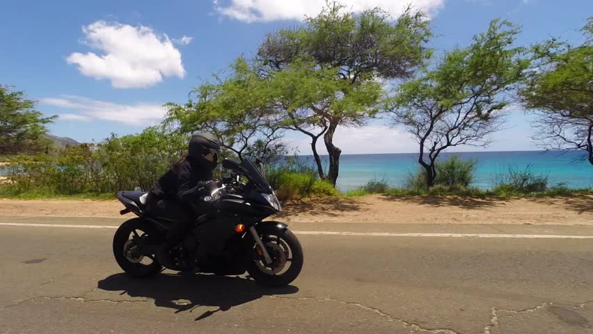 Female biker, dressed in all black, riding bike on a sunny day with blue skies on the west coast of Oahu, Hawaii, passing by beaches and sand