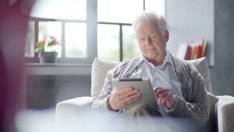 old man is using tablet computer at home