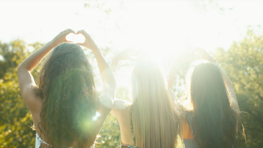 Three young Caucasian teen making heart shapes with their hands. Sun flares. Summer holidays, friendship concept. Blackmagic URSA Mini RAW graded footage