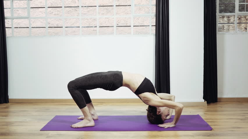 Yoga professional gymnast training exercising in gym, slow motion.A woman practicing yoga,performingstretches routines and exercizes in closed gym in 50fps slow motion.Occasional slider/dolly motion.