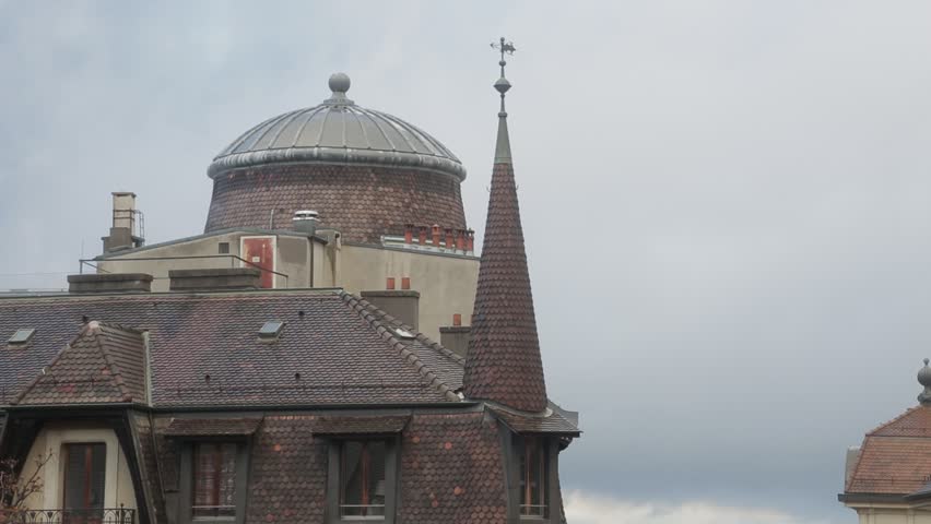 Tile roofs and windows of the buildings in the old town in Geneva, Switzeland. Roof with smoking chimney on rainy cloudy day. Tilt down shot.