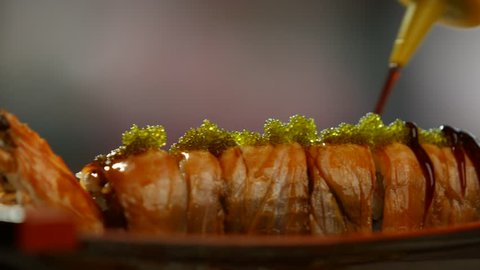 Tool pouring sauce on sushi. Sushi rolls with shrimp. Green caviar and dark sauce. Japanese dish with seafood. Arkistovideo