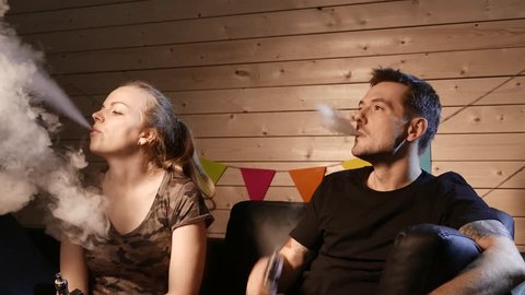 A group of people vaping, inhaling and exhaling large clouds of smoke and having fun together.  Company of good friends. 4K UHD.