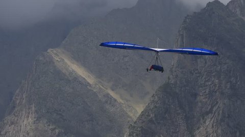 Blue hangglider is trying to gain altitude in a dynamic upward flow near the rocks