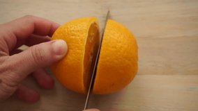 Cutting whole orange on a light wooden cutting board, close up video