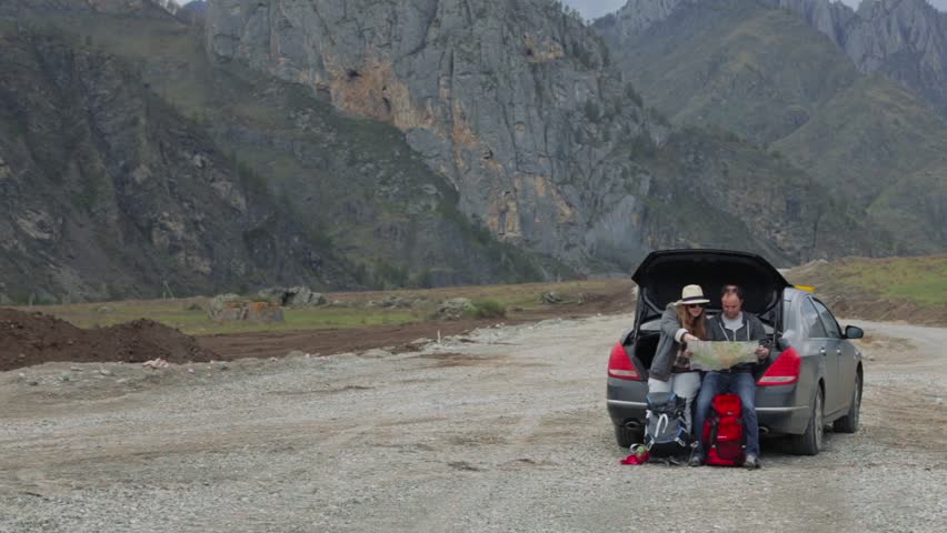 Guests travelling by car stopped somewhere in the mountains and look to the road map.