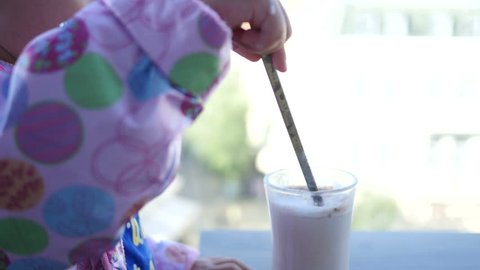 Little girl child in cafe licks the tube from a milkshake - kid drinking milk