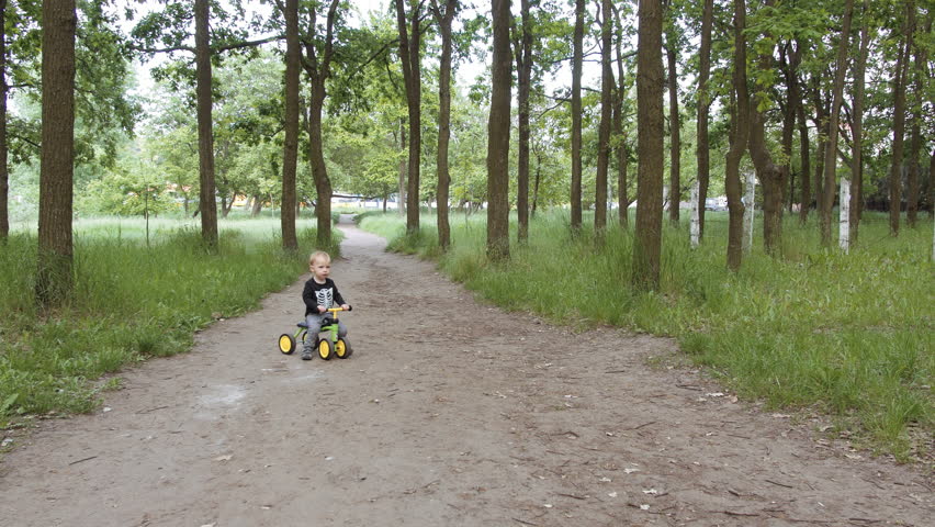 Dolly shot of little boy riding small bike without pedals on road in the park. Happy child on bicycle having fun outdoors in park. Active kid playing, cycling and spending family time.