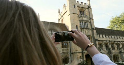 Young woman student taking photo on smartphone of the Magdalen College architecture details - best education atmosphere in the city of Oxford
