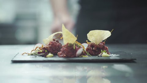 Chef is finishing gourmet meal (raw meat) at commercial kitchen in a restaurant. Close up Arkistovideo