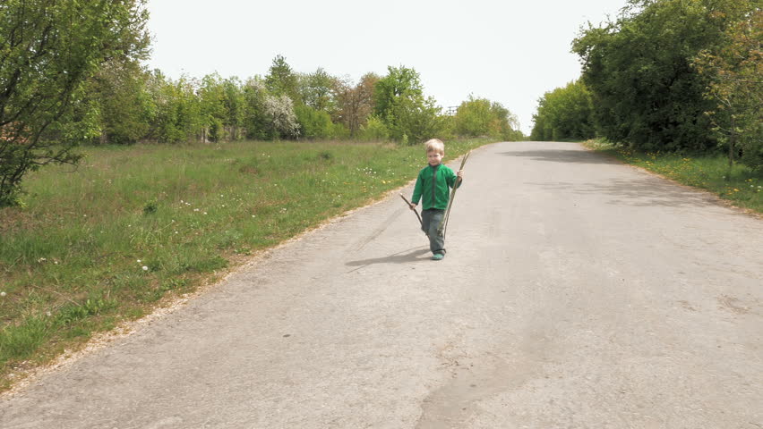 Happy cute little 3-5 years child boy plays outdoor game with rod and walks outdoor on road. Carefree childhood summer and happiness concept. 4K UHD video footage.