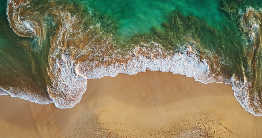 Aerial view waves break on white sand beach at sunset, land meets sea