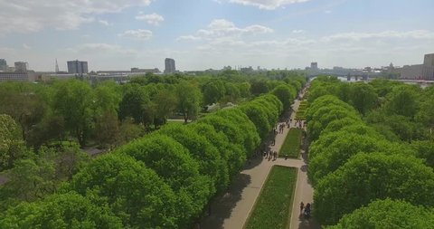 Aerial view of green trees in the park, cityscape, flowerbeds, crowds of people walking on the sidewalks, river bank, Moscow river on sunny summer day. Gorky park, Moscow, Russia.