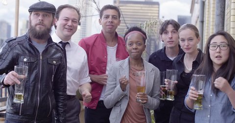 Group of mixed race and gender friends celebrate a victory as an event unfolds off-screen in front of the Downtown Los Angeles skyline at sunset.  Medium shot, recorded in slow motion at 60fps.