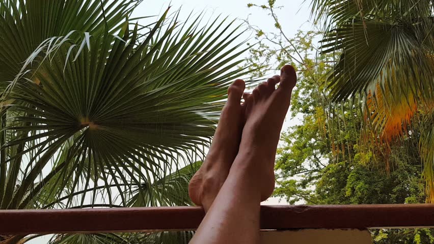 Male legs in a tropical hotel balcony over palm trees