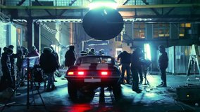 Members of film crew are engaged in installation of equipment round car on set in street