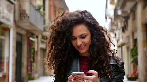 Portrait of young woman with smart phone walking in the city streets, slow motion
