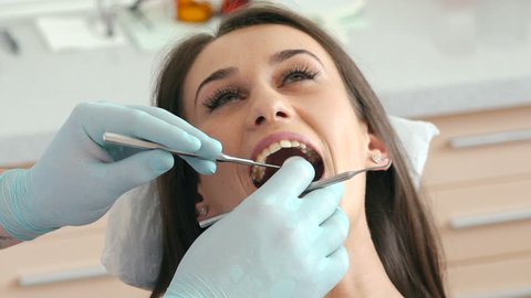 Closeup of dentist examining young pretty woman's teeth