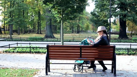 Angry woman with stroller talking on cellphone on bench in the park
