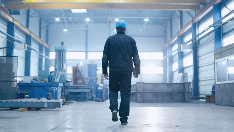 Follow footage of factory worker in a hard hat that is walking through industrial facilities. Shot on RED Cinema Camera.