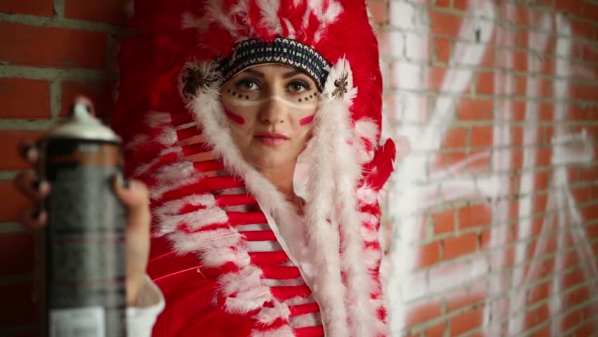 A woman in a bright feather hat holding bottle of paint in front of camera