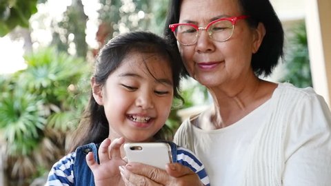 Little Asian girl using smart phone with her grandmother, Happy family concept, Slow motion with pan shot.