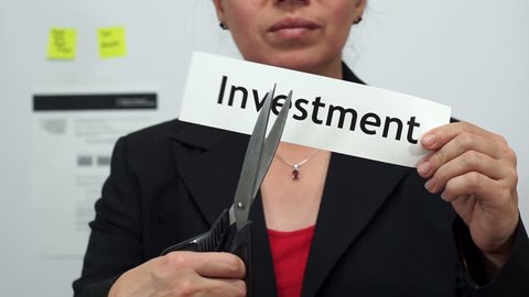 Female office worker or business woman cuts a piece of paper with the word investment on it as an investment reduction business concept.