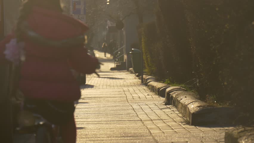 Kid, Silhouette in Sun Rays, Little Girl is Riding the Bike Along a Street in Opole, Poland, Cars Are Parked Along a Street, Child is Riding Away Among the People Walking by a Vintage Street,