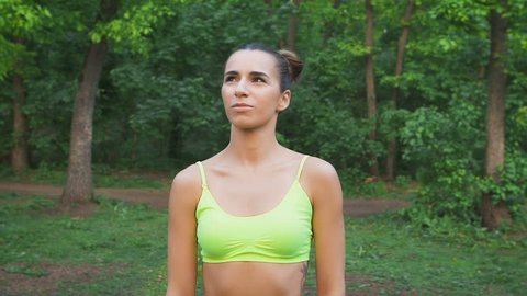 Attractive fitness girl flexing the neck. It is located in the forest, and is preparing to trenerovke. Slow Motion, shot 100 fps