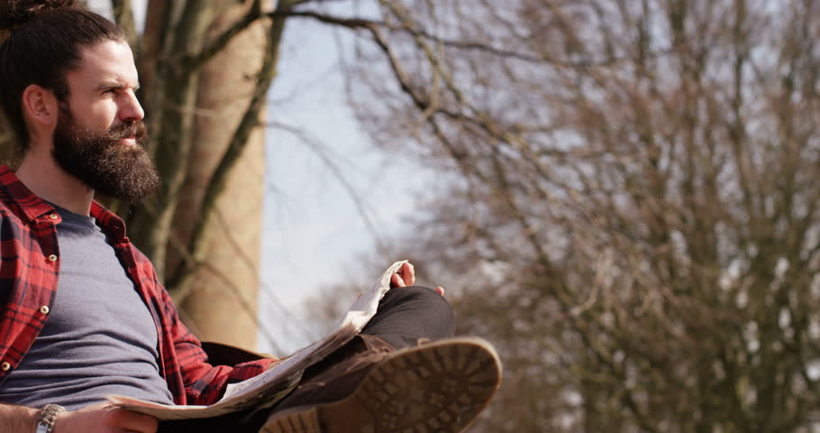 4K Young trendy man enjoying quiet time alone with nature, reading newspaper with his bicycle beside him